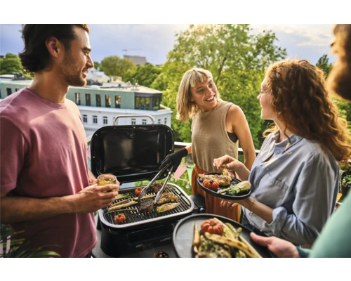 Gruppe von Menschen grillt auf einem Balkon mit einem Holzkohlegrill und Gemüse.
