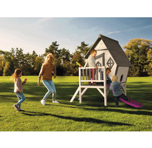 Eine Familie spielt im Garten mit einem Spielhaus mit Rutsche.