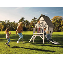 Familie mit Kindern spielt auf einem Holzspielhaus mit Rutsche im Garten.