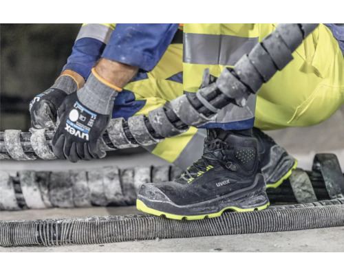 Person mit Arbeitshandschuhen und Sicherheitsschuhen bei der Arbeit mit einem Spiralkabel