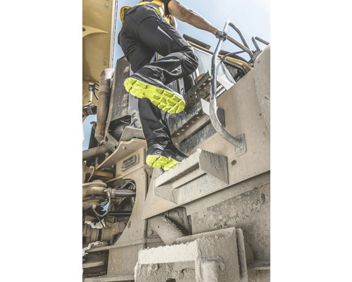 Mann steigt mit Sicherheitsschuhen auf eine Baumaschine.