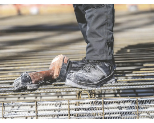 Person mit Arbeitsschuhen und Betonbindegerät auf Bewehrungsgitter