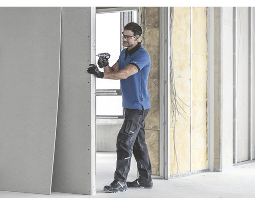 Ein Handwerker befestigt eine Gipskartonplatte mit einem Akkubohrer an einer Wand.