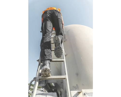 Eine Person mit Arbeitshose und Sicherheitsweste steigt eine Leiter an einem Silo hoch.