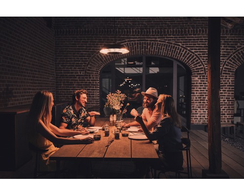 Gruppe von Personen sitzt an einem Holztisch in einem Außenbereich unter einer Heizlampe