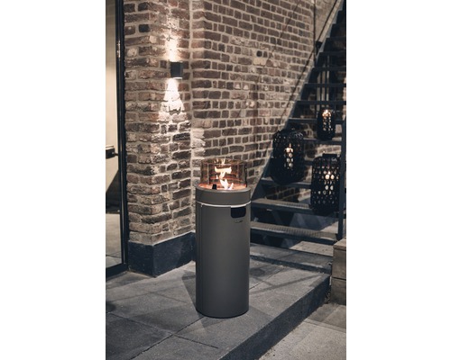 Terrassenheizer mit Flamme und Glasaufsatz vor einer Backsteinwand und Treppe