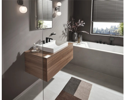 Badezimmer mit Waschtisch aus Holz, Spiegel, Beleuchtung und Badewanne vor einem Fenster