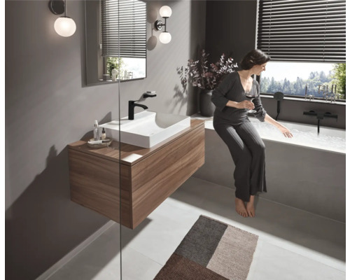 Helles Badezimmer mit Waschtisch, Spiegel, Beleuchtung und Badewanne mit Frau