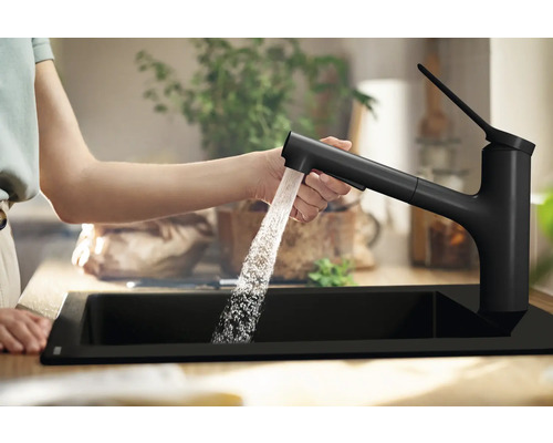 Eine Person bedient eine schwarze Küchenarmatur mit Ausziehbrause über einem schwarzen Spülbecken.