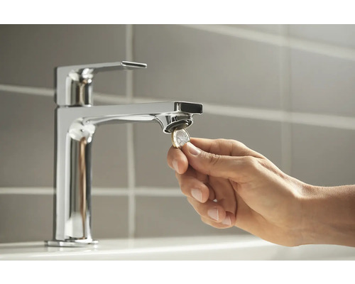 Eine Hand wechselt mit einer Münze den Strahlregler eines Wasserhahns.