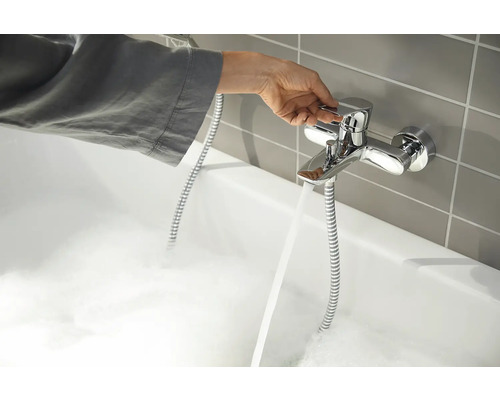 Hand bedient einen Wasserhahn an einer mit Schaum gefüllten Badewanne