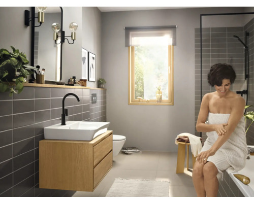 Helles Badezimmer mit Waschtisch, Spiegel, Dusche und einer Frau mit Handtuch