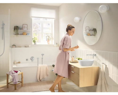 Helles Badezimmer mit ovalem Spiegel, Waschtisch und Badewanne.