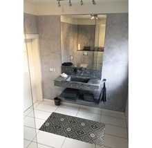 Badezimmer mit Waschbecken aus Stein, Spiegel und gemusterter Badematte