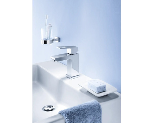 Badezimmerwaschbecken mit Armatur, Seife, Seifenschale, Handtuch, Zahnputzbecher und Zahnbürste.