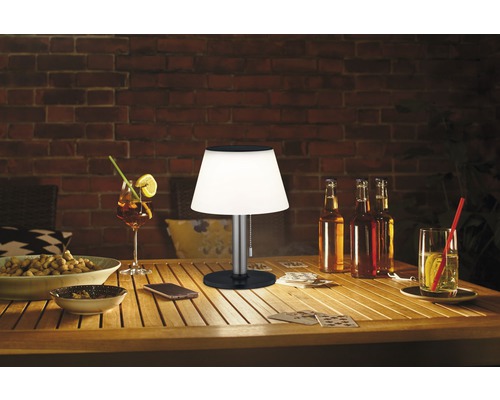 Tischszene mit Getränken, Snacks und einer Tischleuchte auf einem Holztisch im Freien.