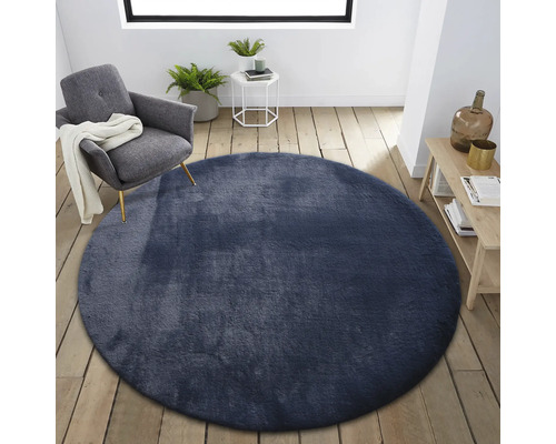 Szene mit rundem, textilem Teppich in einem hellen Raum mit Sessel, Beistelltisch und Holzregal.