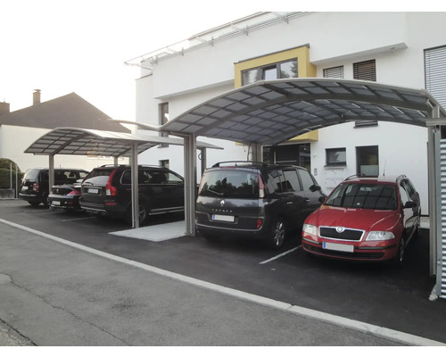 Mehrere unter einem Carport geparkte Autos vor einem Gebäude.