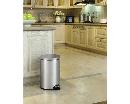 Silberfarbener Treteimer in einer Küche mit hellen Holzschränken und Fliesenboden.