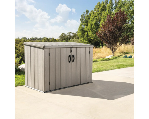 Mülltonnenbox Lifetime inkl. Gasdruckfedern 191 x 109 x 131 cm braun Graue Gartenbox auf einer Terrasse mit Bäumen und Rasen im Hintergrund.