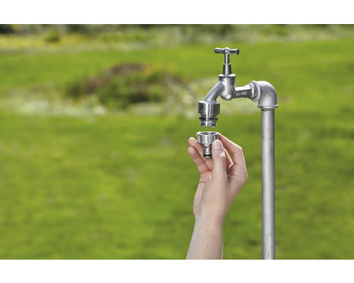 Außenwasserhahn mit Schnellkupplung in der Hand vor grünem Hintergrund