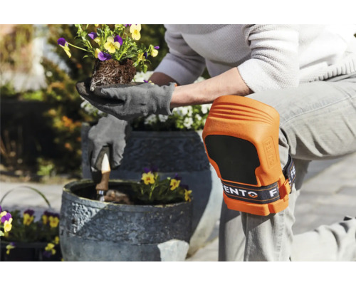 Person mit Knieschützern und Gartenhandschuhen pflanzt Blumen in einen Topf
