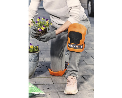 Eine Person mit Knieschonern pflanzt Blumen im Garten.