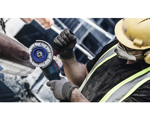 Ein Bauarbeiter schleift mit einem Winkelschleifer ein Metallrohr.