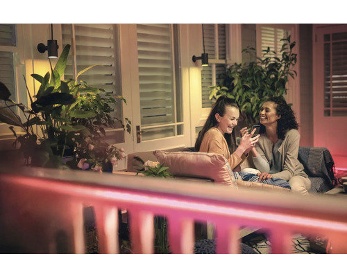 Zwei Frauen sitzen auf der Terrasse unter Wandleuchten und Zimmerpflanzen.