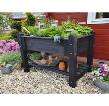 Hochbeet aus Holz mit Kräutern, Gartengeräten und Ablagefläche im Garten.
