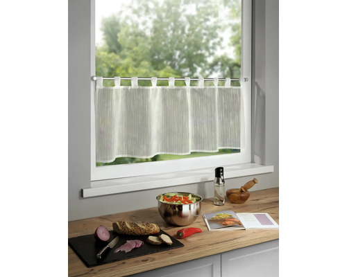 Gardinenstore vor einem Fenster, dazu Zutaten für eine Mahlzeit auf einer Küchentheke