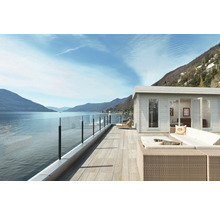 Szene mit Gartenhaus, Terrasse mit Glasgeländer, Loungemöbeln und Blick auf einen See.