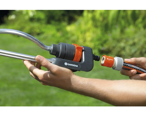 Person verbindet einen Gartenschlauch mit einem Regner von Gardena.