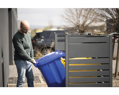 Eine Person stellt eine blaue Mülltonne in eine graue Mülltonnenbox.