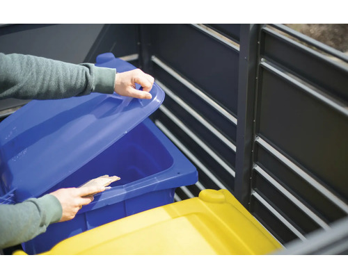 Eine Person öffnet den Deckel einer blauen Mülltonne in einer Mülltonnenbox.