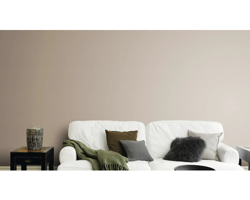 Wohnzimmer mit weißem Sofa, Kissen, Decke und dekorativer Vase auf einem Beistelltisch vor einer einfarbigen Wand