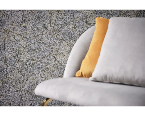 Nahaufnahme einer grauen Strukturtapete mit einem geometrischen Linienmuster neben einem Sofa mit Kissen