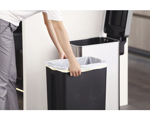 Eine Person wechselt den Müllbeutel in einem Abfalleimer in der Küche.