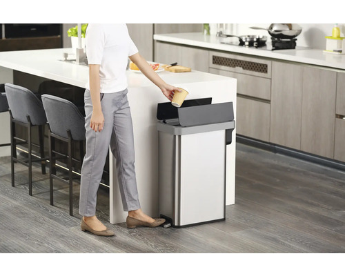 Frau wirft Becher in einen Edelstahl-Treteimer in einer Küche
