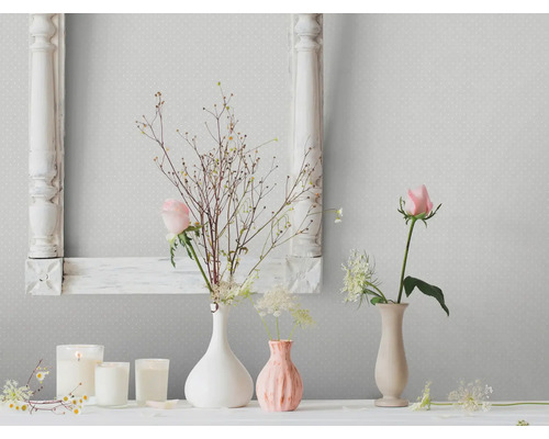 Wohnraum-Szene mit floralen Dekorationen, Kerzen und einem Bilderrahmen vor einer gemusterten Tapete