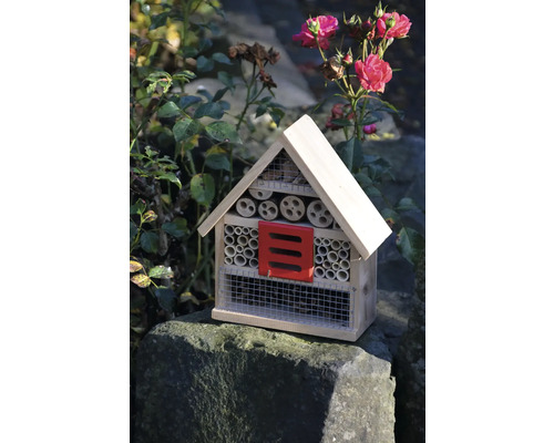Insektenhotel aus Holz mit rotem Element und verschiedenen Füllmaterialien im Garten