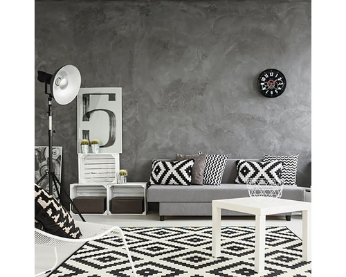 Wohnzimmer mit grauer Wand, Sofa mit Kissen, Teppich mit geometrischem Muster und weißem Couchtisch.