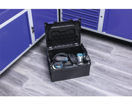 Geöffnete Werkzeugkiste mit Elektrowerkzeugen vor blauen Metallschränken