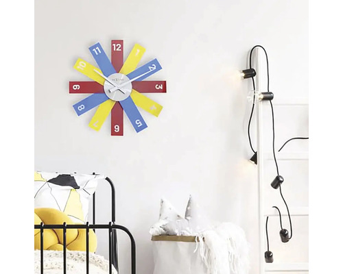 Szene mit einer Wanduhr mit bunten Ziffernblättern, einer Leiter mit Glühbirnen und einem Bett.