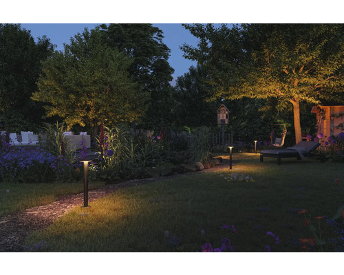 Beleuchteter Garten mit Außenleuchten, Gartenmöbeln und Pflanzen bei Nacht.