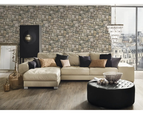 Wohnzimmer mit Ecksofa, Steintapete, Ottomanenhocker, Schrank und Dekorationsgegenständen.