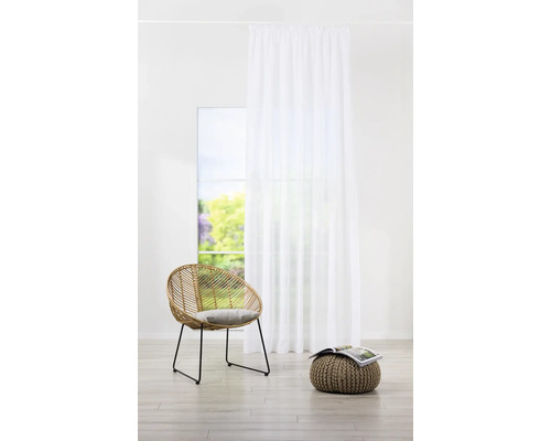 Helles Zimmer mit weißem Vorhang, Rattansessel und Pouf mit Zeitschrift