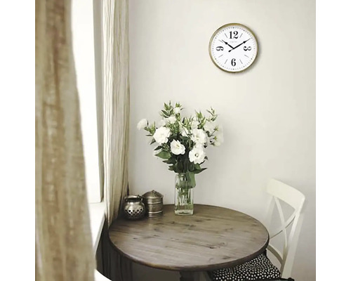 Helles Interieur mit einem runden Holztisch, einer Vase mit weißen Blumen und einer Wanduhr