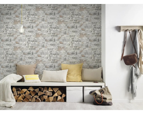 Wohnraum mit gemusterter Tapete in Backsteinoptik, Sitzbank mit Kissen, Holzscheiten und Dekoration