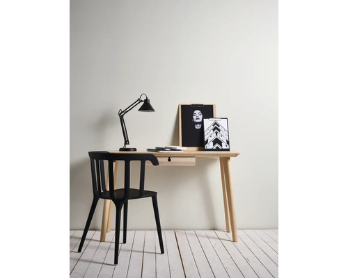 Ein Schreibtisch mit Schublade, Lampe, Bildern und einem schwarzen Stuhl.